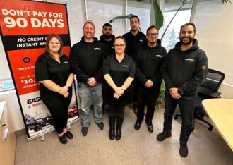 autologiQ team photographed beside a Don't Pay for 90 Days promotional banner
